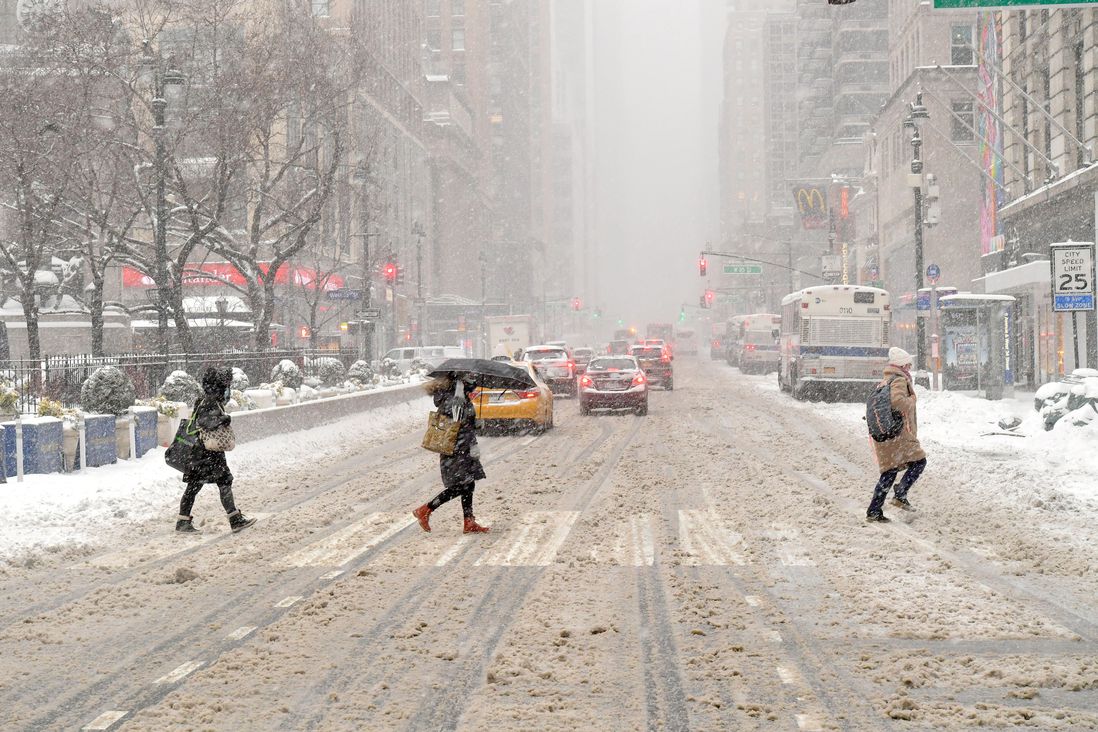 Pedestrians cross a very slushy street with snow coming down